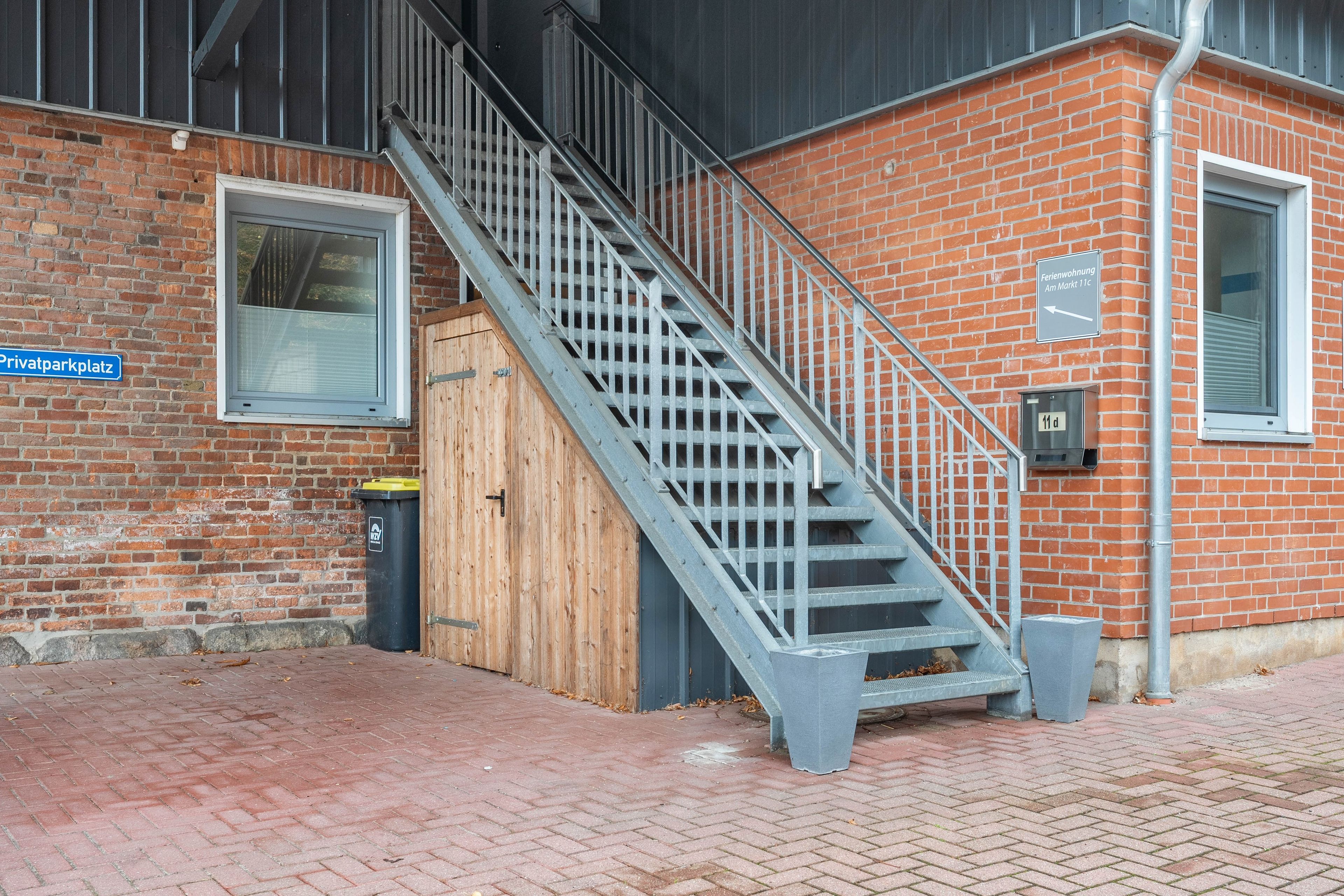 Eine Treppe führt zu einer Holztür, einem Mülleimer und einem Ziegelgebäude mit einem Fenster und einem Schild.