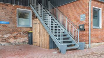 Eine Treppe führt zu einer Holztür, einem Mülleimer und einem Ziegelgebäude mit einem Fenster und einem Schild.