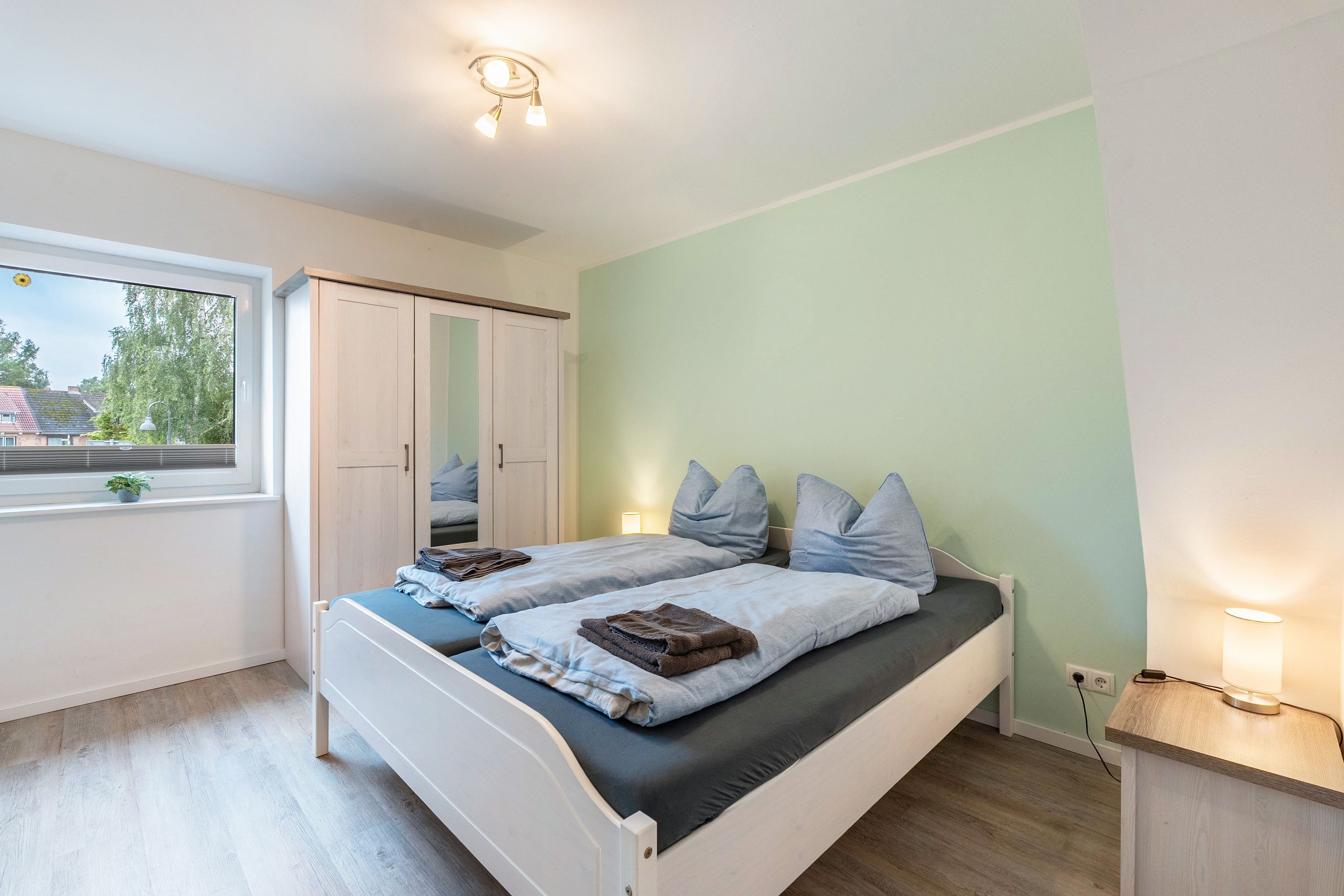 A bedroom with a bed, bedside lamps, a window, and a wardrobe.