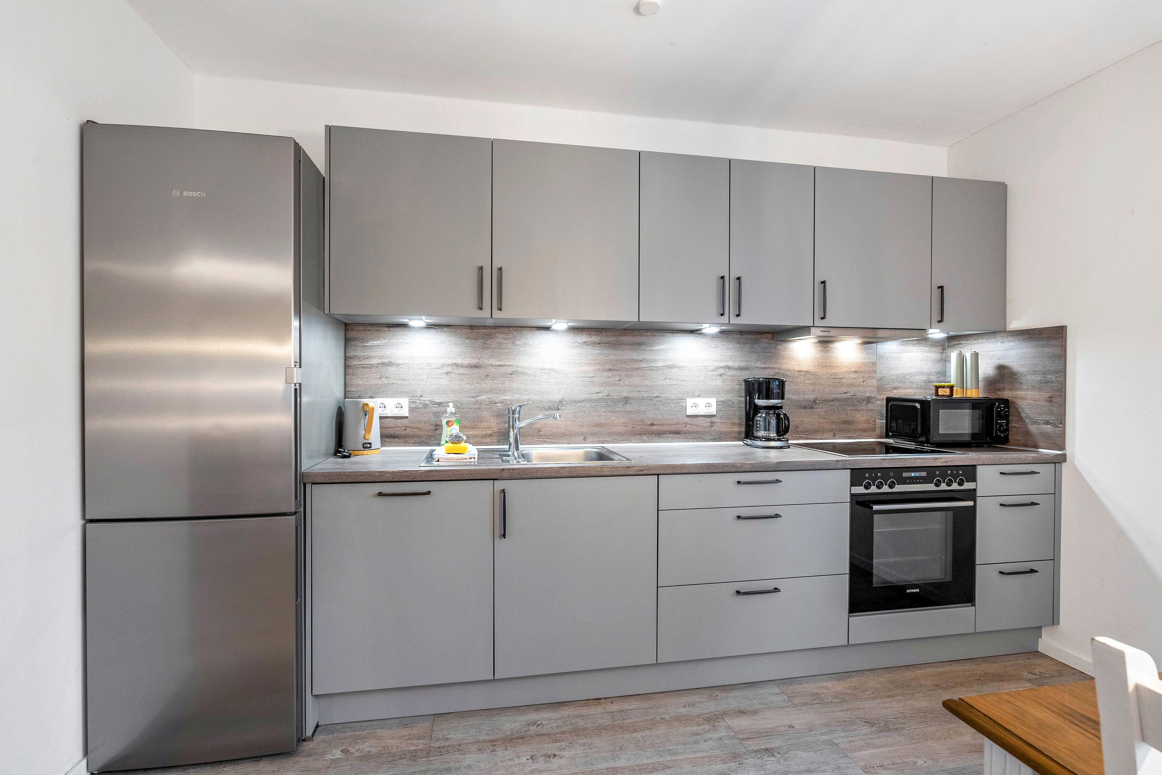 Une cuisine moderne avec des meubles gris, des appareils en acier inoxydable et un plan de travail en bois.