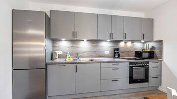 Une cuisine moderne avec des meubles gris, des appareils en acier inoxydable et un plan de travail en bois.