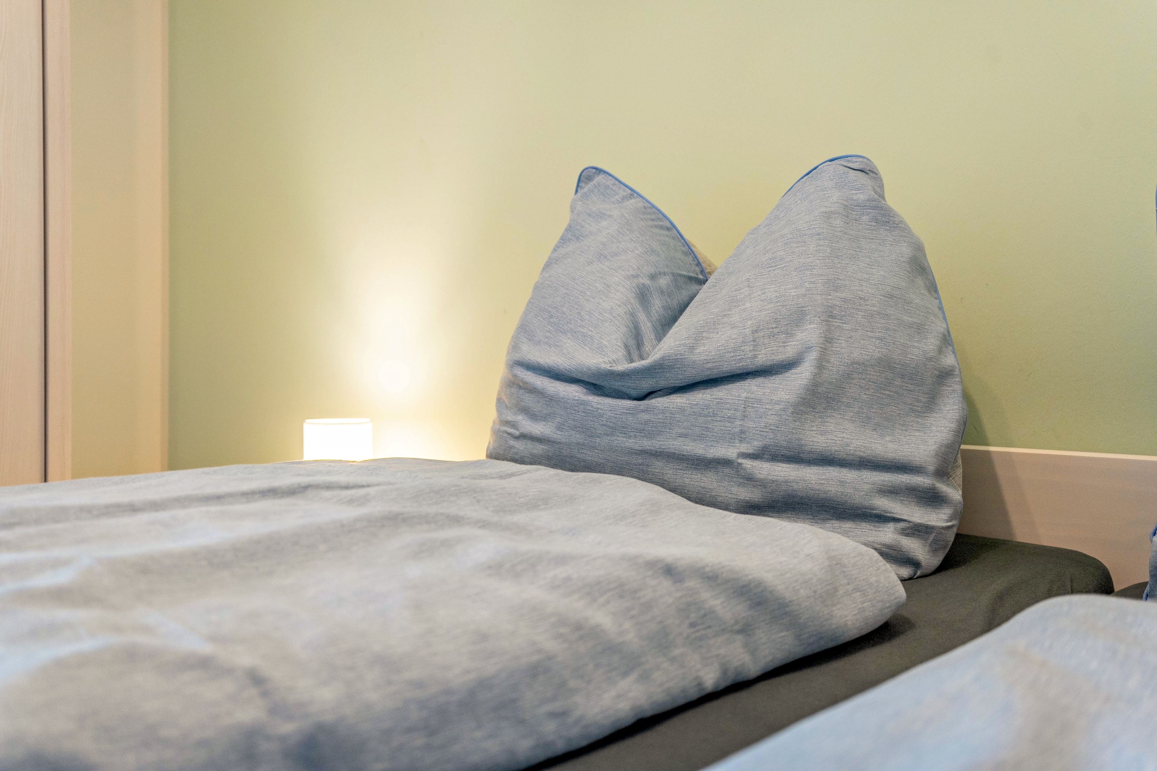 A bed with a grey blanket and two grey pillows.