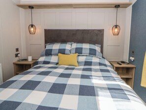 A bed with a checkered bedspread, a headboard, bedside tables, and two wall-mounted lamps. - Santa Maria (Llandysul)