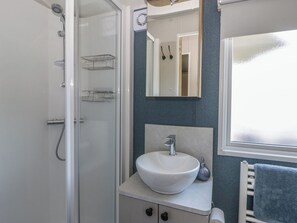 A bathroom with a glass shower enclosure, a white sink with a vessel basin, a towel rack, and a mirror above the sink. - Santa Maria (Llandysul)