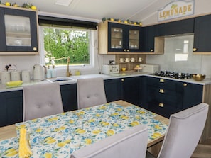 A kitchen with a table set for dining, a window with a view, and a sign reading 'LEMONADE'. - Santa Maria (Llandysul)