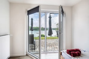 Een kamer met een schuifdeur naar een terras buiten, met uitzicht op een meer en parasols.