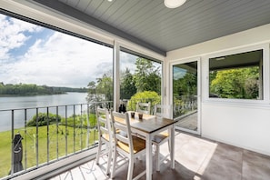 En balkong med ett bord och stolar, med utsikt över en sjö och grönområden.