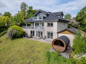 Een huis met twee verdiepingen, een balkon, een houten vat en een verzorgde tuin.