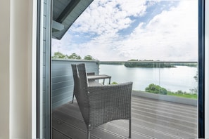 A balcony with a wicker chair and table, overlooking a calm body of water and a distant shoreline. - Holiday Home 'Haus Am See' with Lake View, Private Terrace and Wi-Fi (Stocksee)