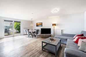 Ett modernt vardagsrum med en grå soffa, ett soffbord, en tv och en matplats med stolar och ett bord.