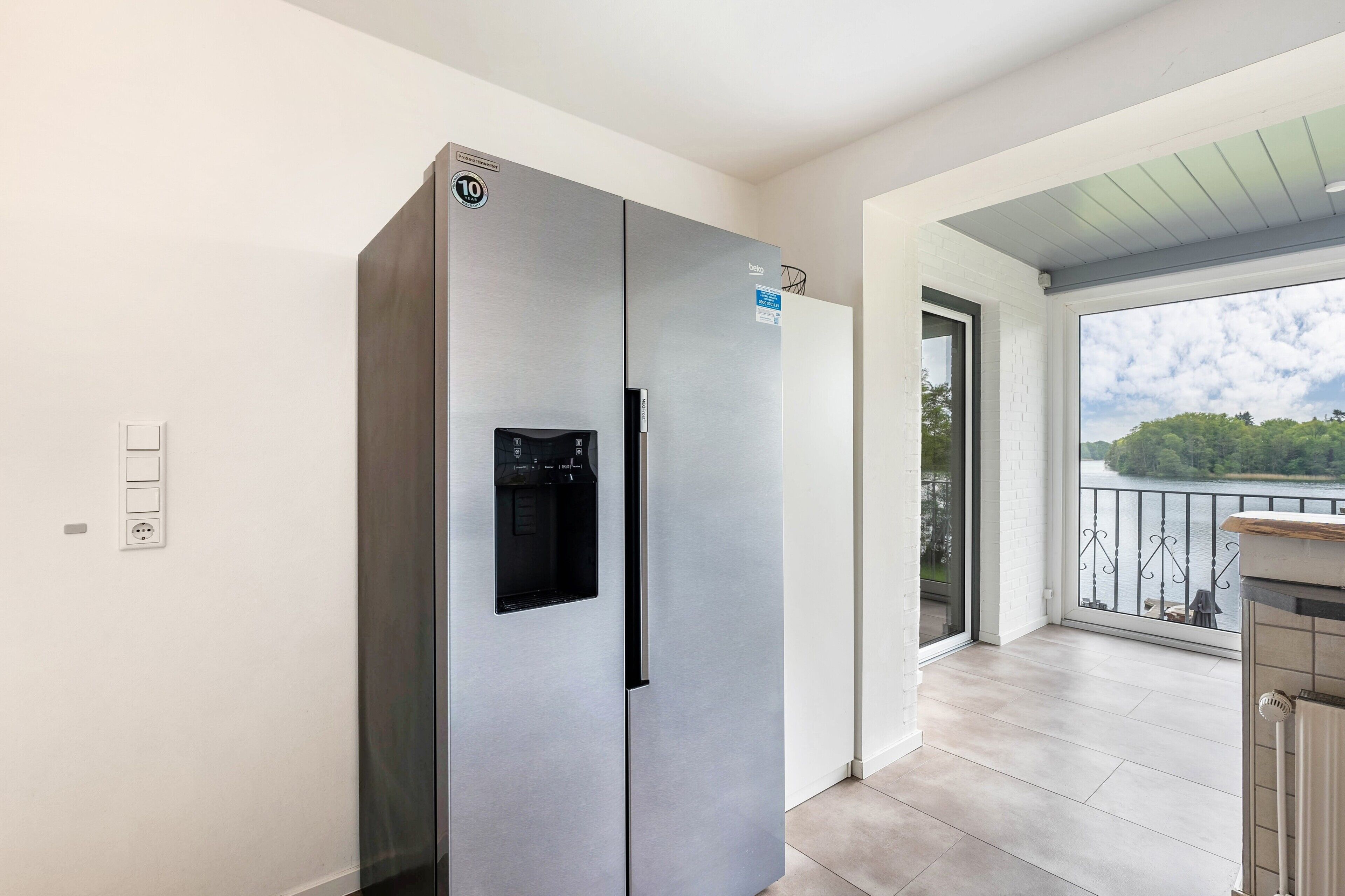 A modern kitchen with a stainless steel refrigerator, a water dispenser, and a view of a balcony with a railing.