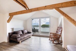 Une pièce de style loft avec un plafond en bois, une porte-fenêtre coulissante donnant sur un balcon, un canapé en cuir marron et un fauteuil à bascule.