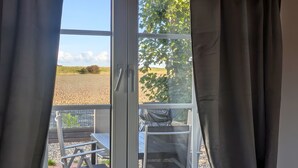 Ein Zimmer mit Blick auf ein Kiesfeld und Bäume durch ein Fenster mit Vorhängen.