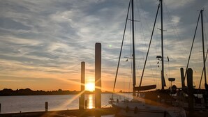 Ein Hafen mit vertäuten Booten, ein Sonnenuntergang im Hintergrund und ein klarer Himmel.
