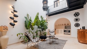 Ein modernes Interieur mit einer Sitzecke, großen Pflanzen und einer durch einen Bogen sichtbaren Küche.