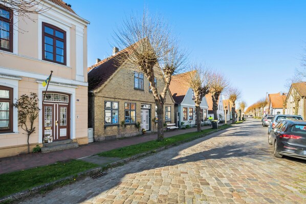 Una calle empedrada flanqueada por edificios de estilo europeo tradicional, un cielo despejado y coches estacionados.