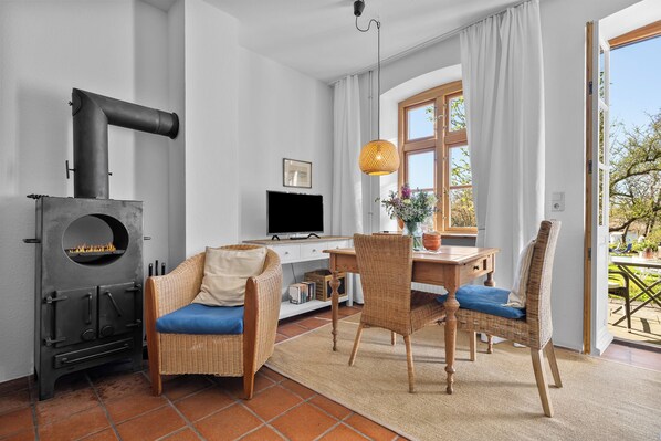 A living room with a wood-burning stove, wicker furniture, a television, and a view of the outdoors. - Wohnen am Noor - fireplace, terrace, access to the jetty directly on the Noor (Arnis)
