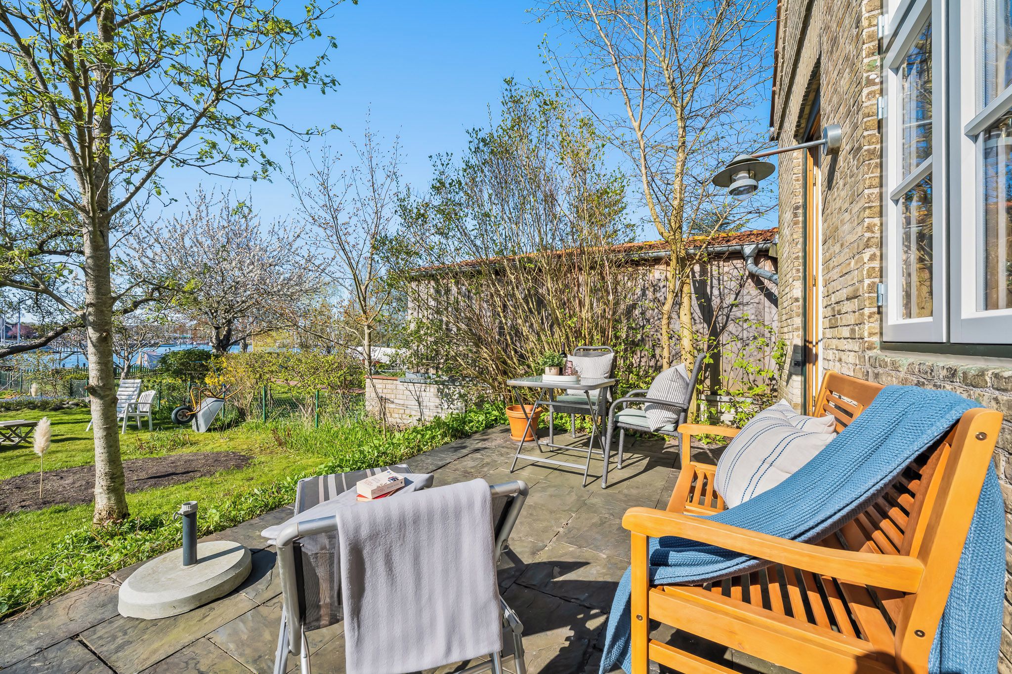An outdoor seating area with a table and chairs, a bench, and a garden with trees and a brick wall.