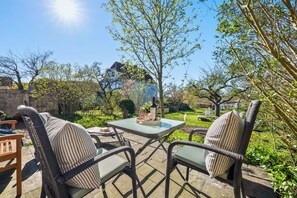 An outdoor patio with wicker furniture and a table, surrounded by greenery and a clear sky. - Wohnen am Noor - fireplace, terrace, access to the jetty directly on the Noor (Arnis)