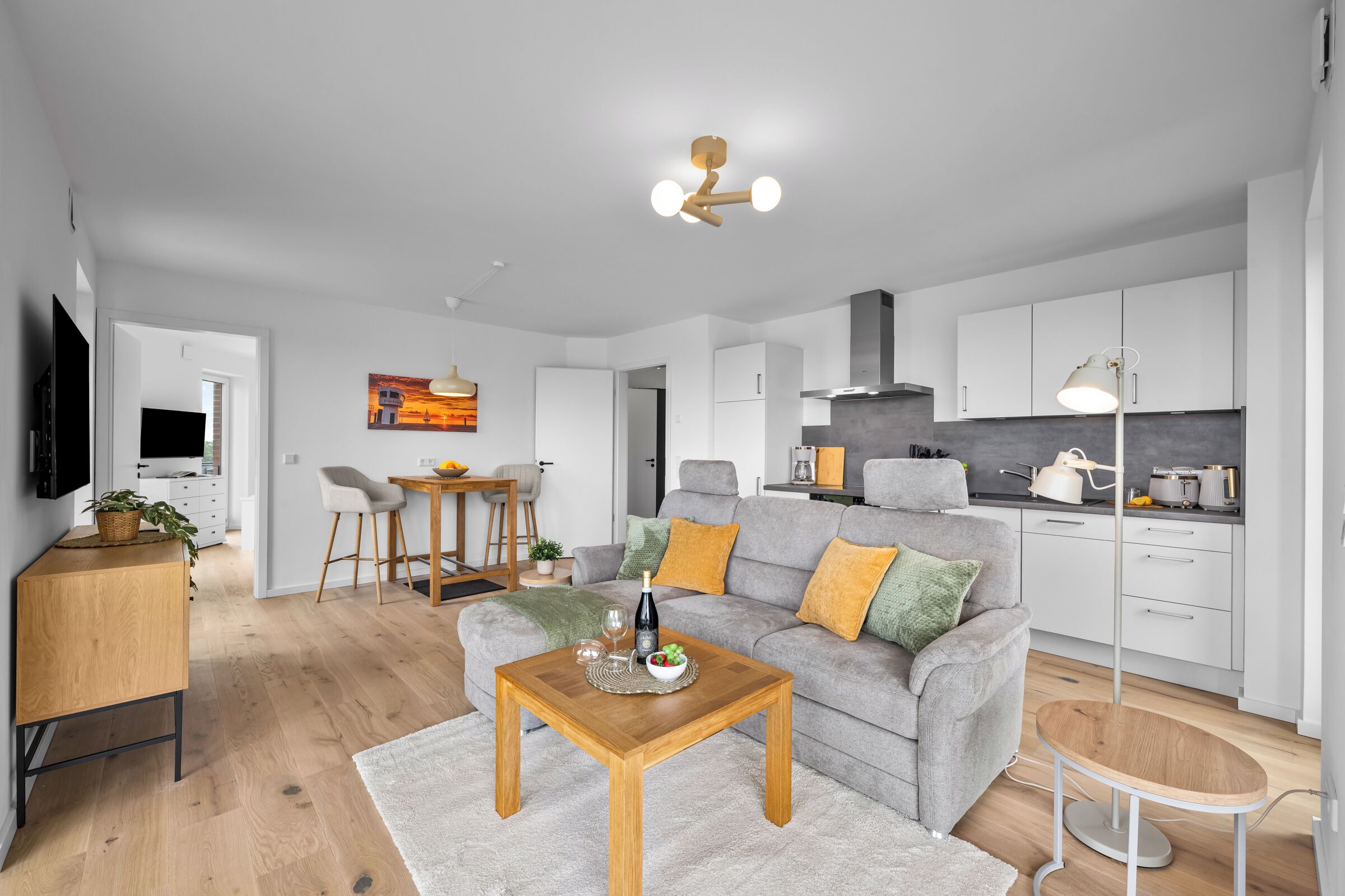 Ein modernes Wohnzimmer mit grauem Sofa, Couchtisch aus Holz und einem Fernseher links.