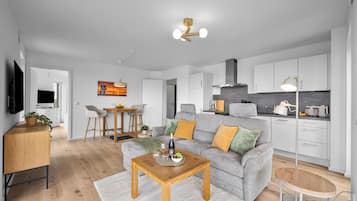 Ein modernes Wohnzimmer mit grauem Sofa, Couchtisch aus Holz und einem Fernseher links.