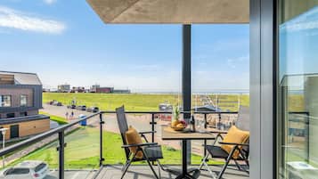 Ein Balkon mit zwei Stühlen, einem Tisch und einer Weinflasche mit Blick auf einen Strand und einen Parkplatz.