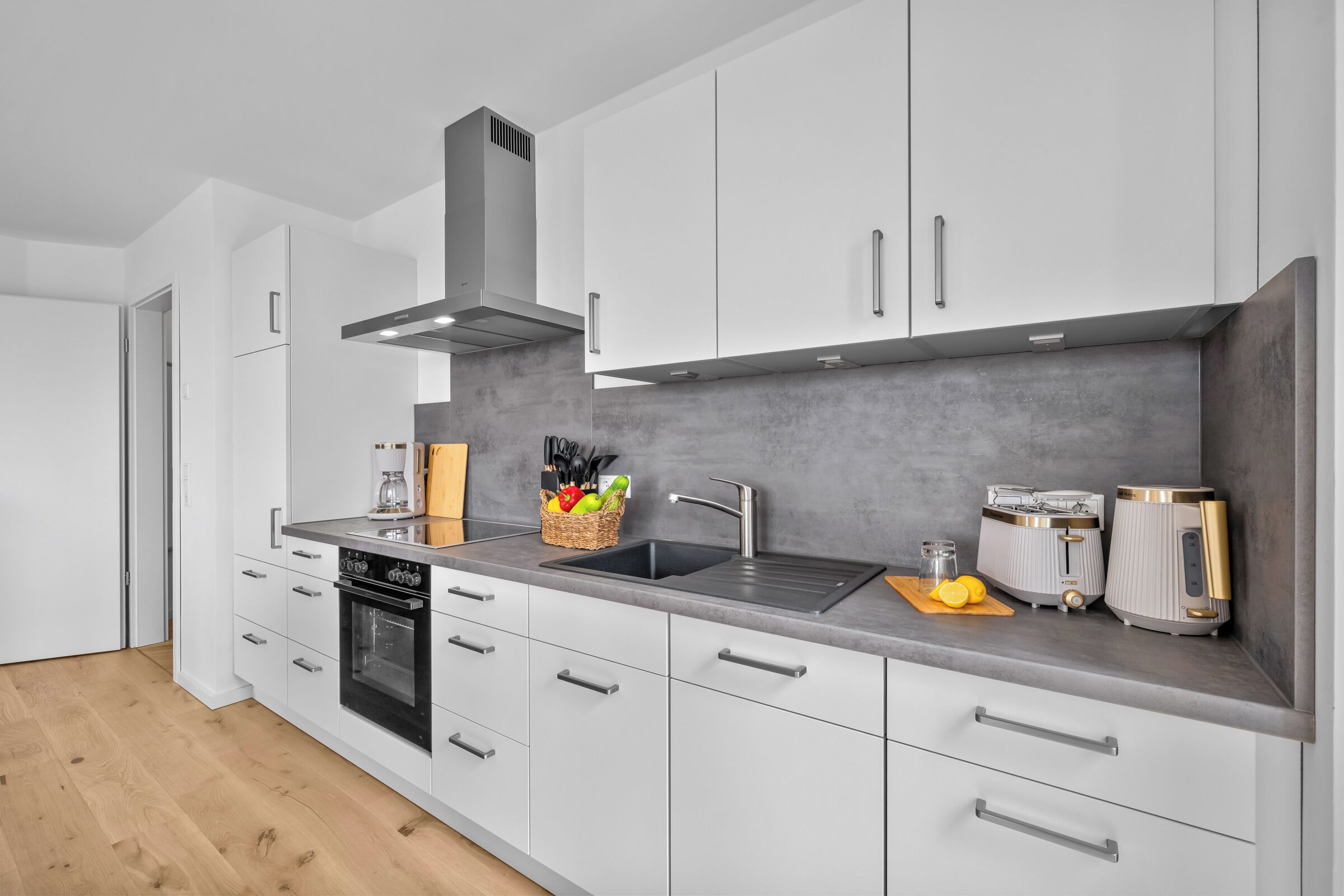 A modern kitchen with white cabinets, a grey backsplash, stainless steel appliances, and a wooden countertop.