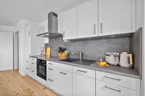 A modern kitchen with white cabinets, a grey backsplash, stainless steel appliances, and a wooden countertop. - The View A08 Belvedere Nordsee - Balcony,sea view,garden furniture,shared. Sauna (Dagebüll)