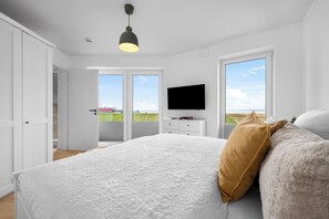 A bedroom with a large bed, a television on a dresser, and a view of the beach through the windows. - The View A08 Belvedere Nordsee - Balcony,sea view,garden furniture,shared. Sauna (Dagebüll)