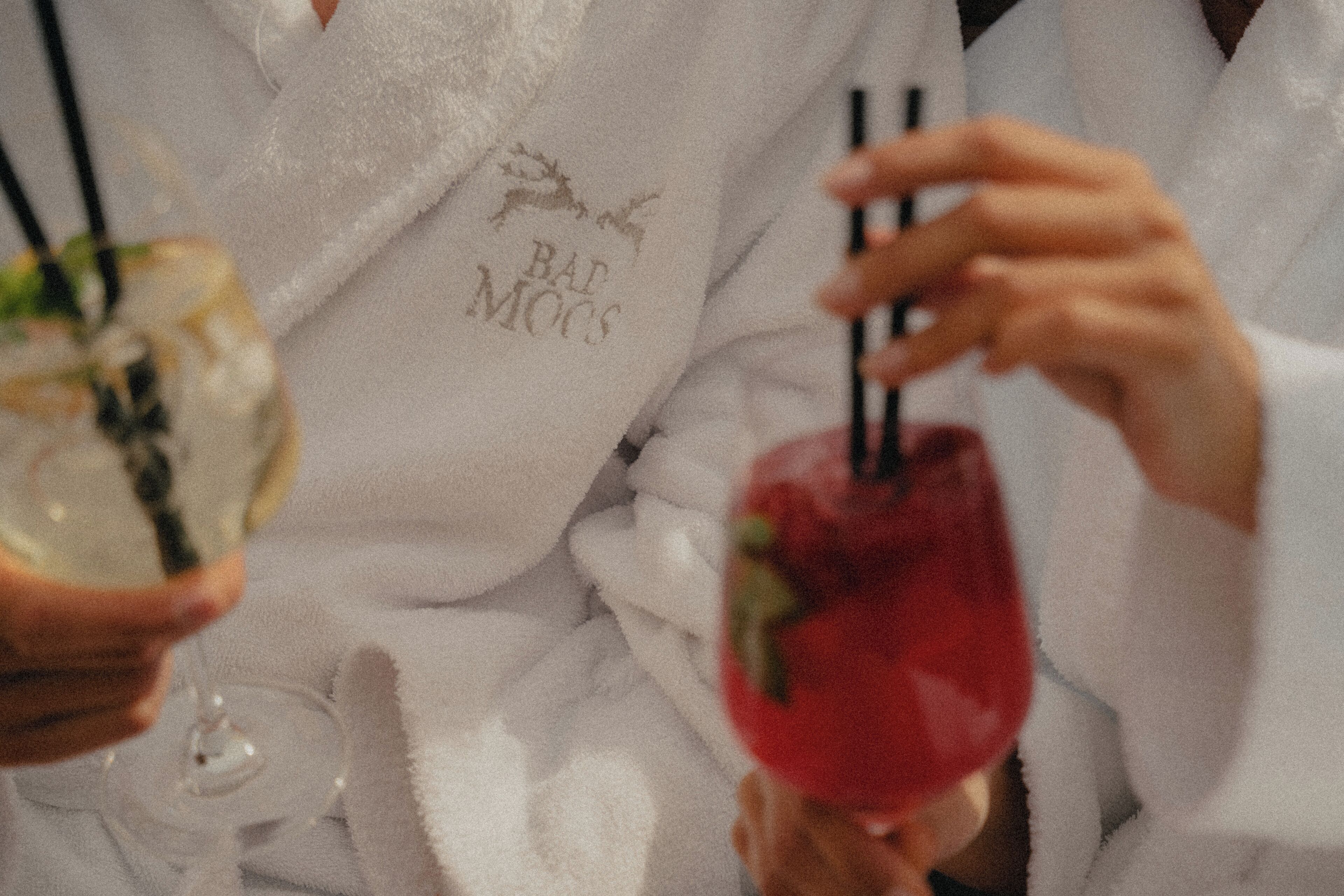 A person holding a cocktail glass with a red drink and a straw, and another glass with a clear drink.