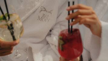 A person holding a cocktail glass with a red drink and a straw, and another glass with a clear drink.