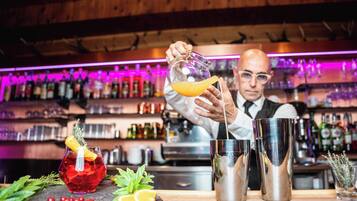 A bartender preparing a drink with a cocktail shaker and a glass on a bar counter, surrounded by various bottles and bar tools.