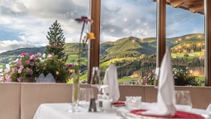 Ein Esstisch für zwei Personen mit Blick auf eine Berglandschaft durch große Fenster.