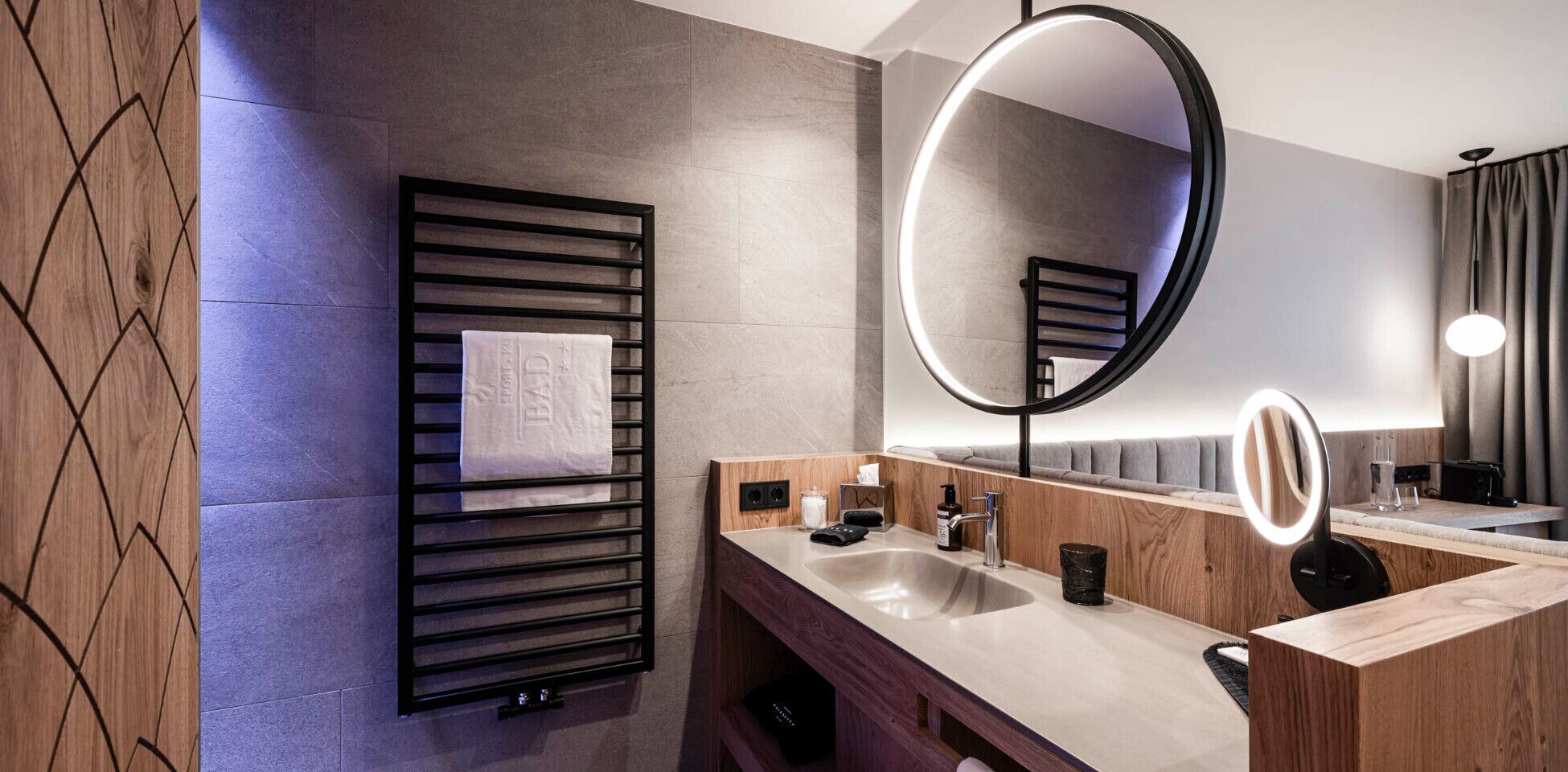Une salle de bain moderne équipée d’un porte-serviettes, d’un lavabo, d’un miroir et d’un luminaire rond.