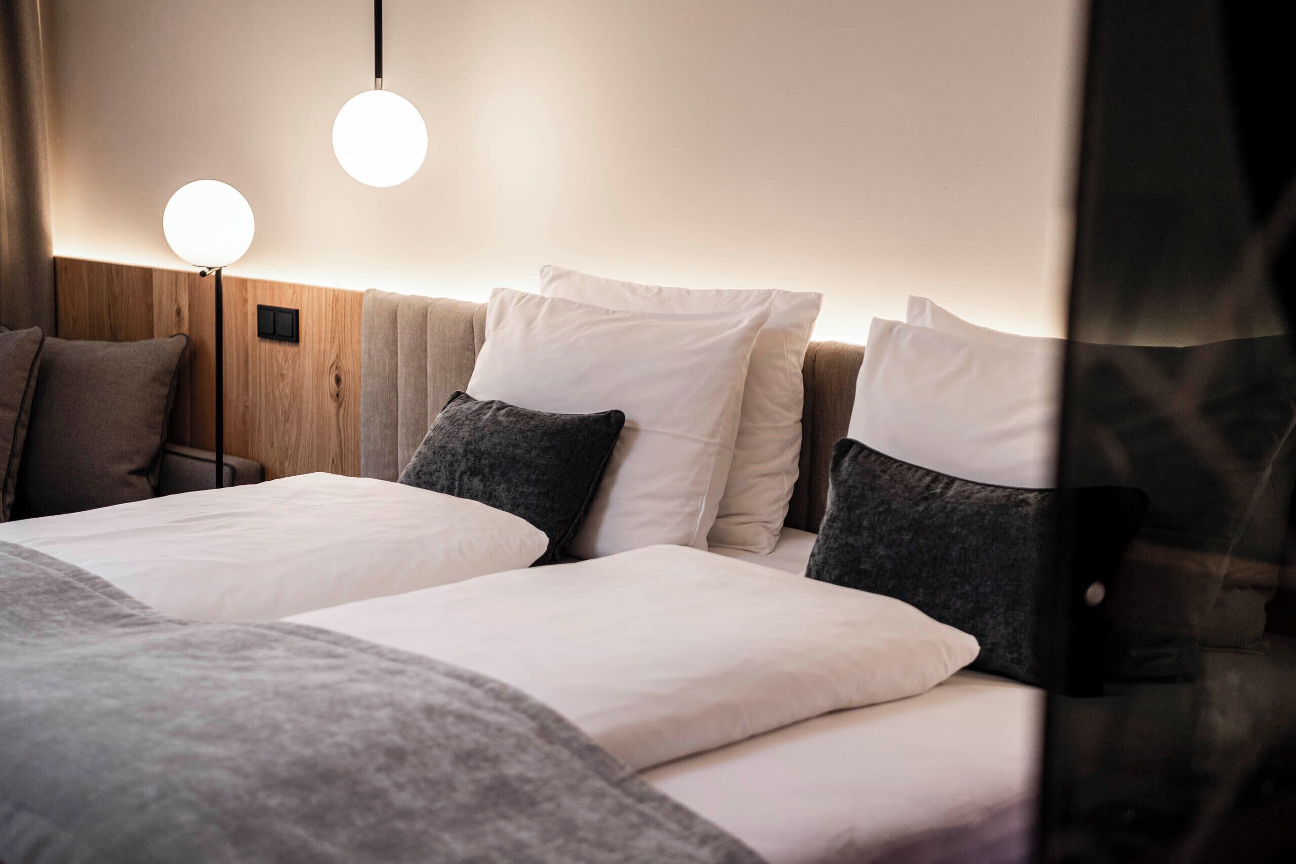 Ein Hotelzimmer mit zwei Betten, einem hölzernen Kopfteil und zwei runden Wandlampen.