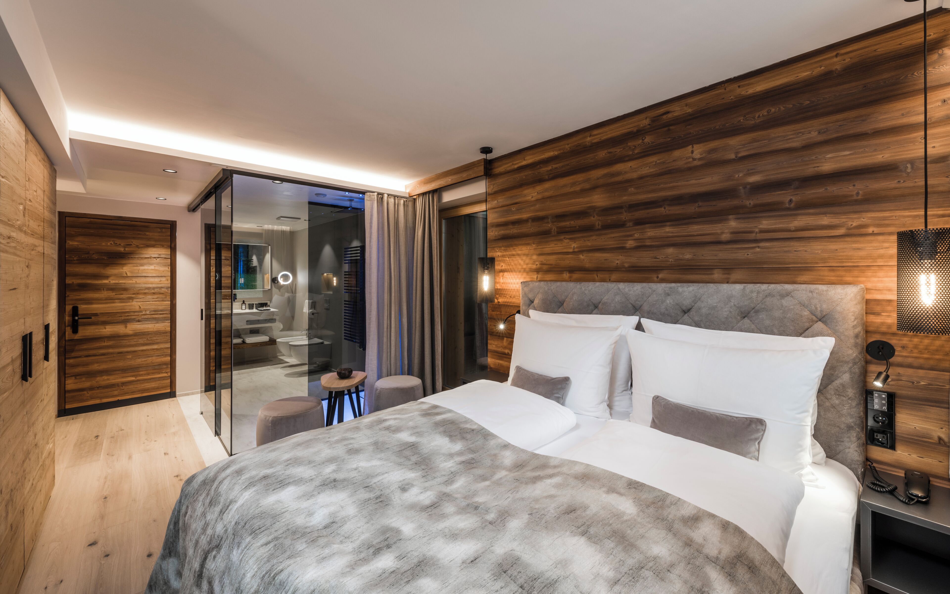 A modern bedroom with a large bed, wooden paneling, a glass shower enclosure, and a visible bathroom.