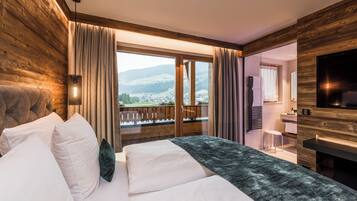 A hotel room with a bed, a TV, a bathroom, and a balcony with a view of the mountains.