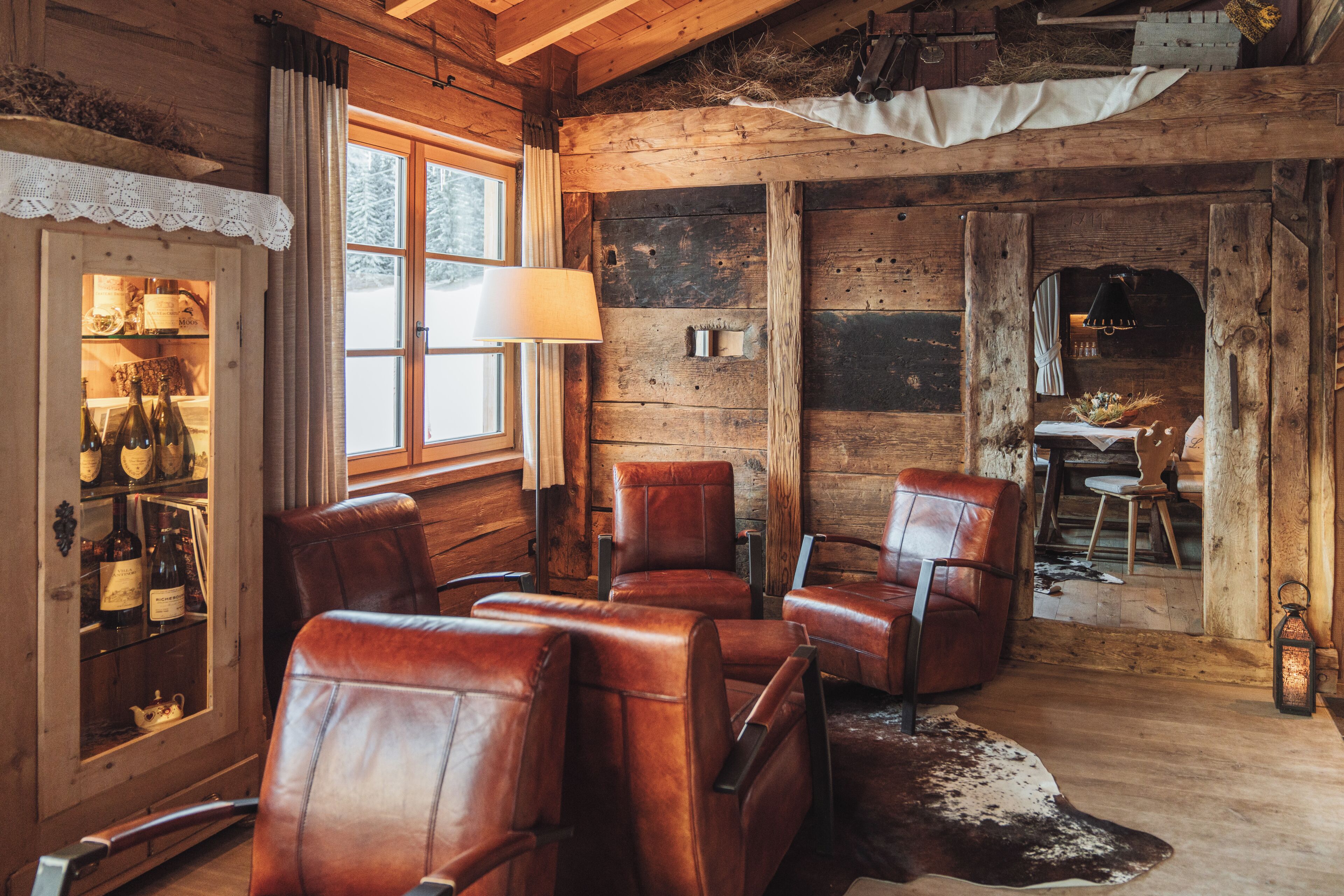A rustic wooden interior with leather chairs, a glass cabinet with bottles, and a cowhide rug.