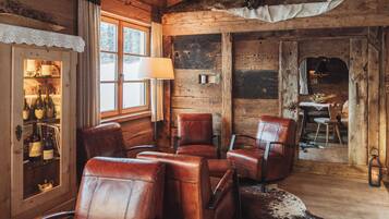 A rustic wooden interior with leather chairs, a glass cabinet with bottles, and a cowhide rug.
