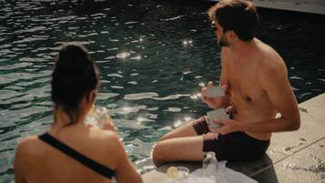 Dos personas sentadas junto a una piscina, con una mesa entre ellas.