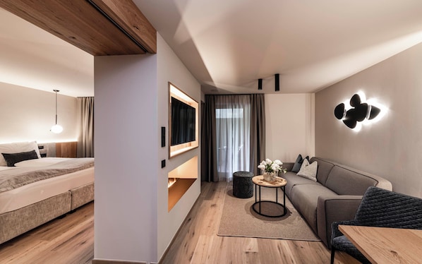 A modern hotel room with a bed, sofa, and a small table with a vase of flowers. - Bad Moos Aqua Spa Resort (Sesto)