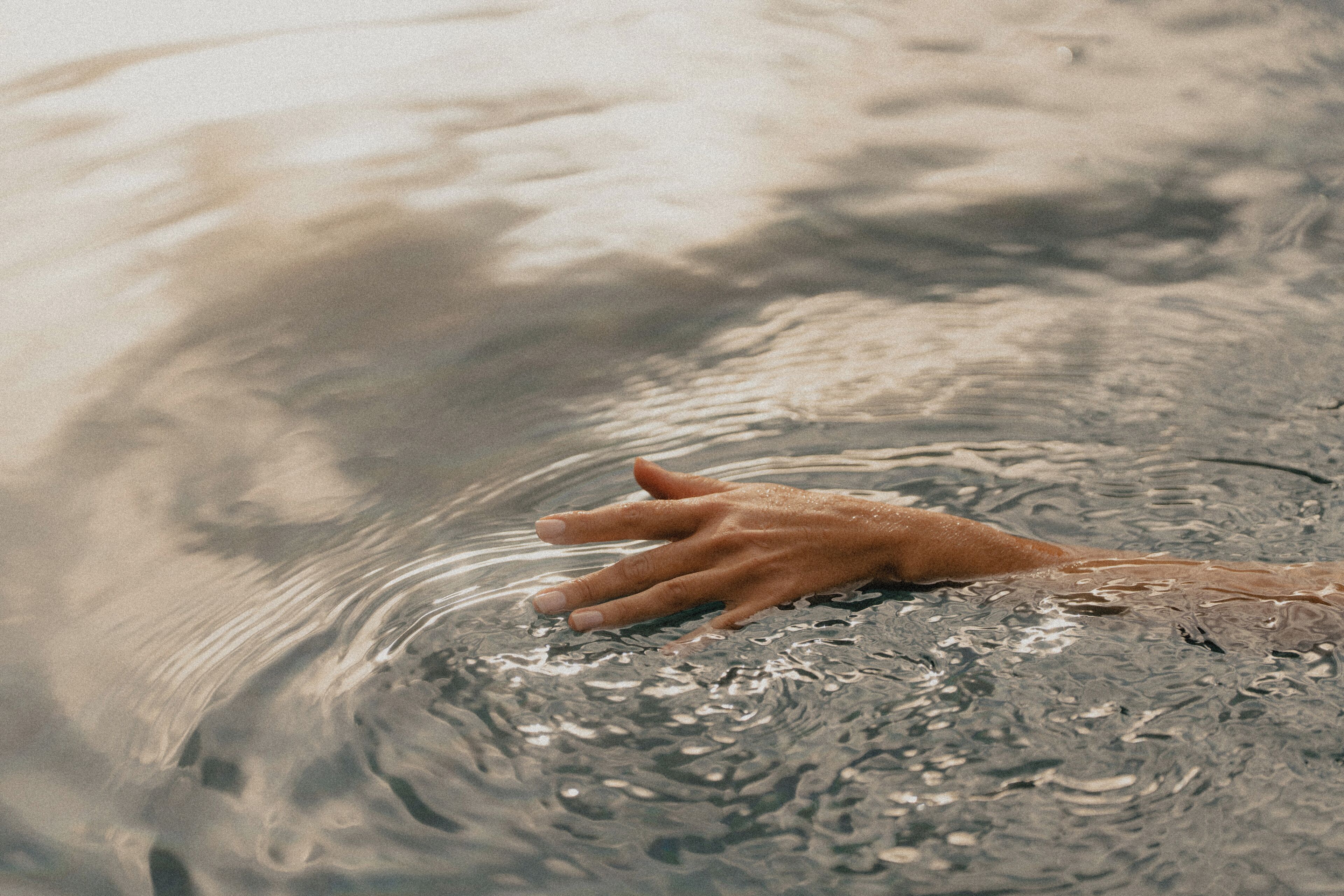 A hand partially submerged in water with ripples around it.