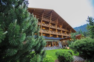 Una cabaña de madera de varios pisos con balcones, rodeada de árboles de hoja perenne y un jardín cuidado.