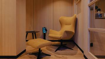 Une chambre moderne avec un plancher en bois, un fauteuil jaune, un pouf assorti et une petite table sur laquelle se trouve un appareil numérique.