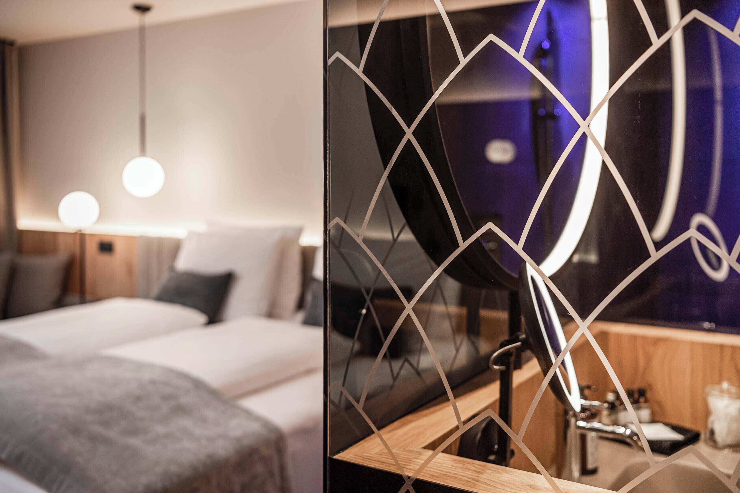 Una habitación de hotel moderna con cama, mesita de noche y espejo de diseños geométricos.