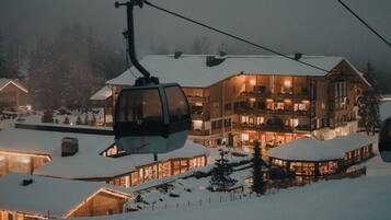 A snow-covered building with multiple balconies, a ski lift, and a well-lit interior.