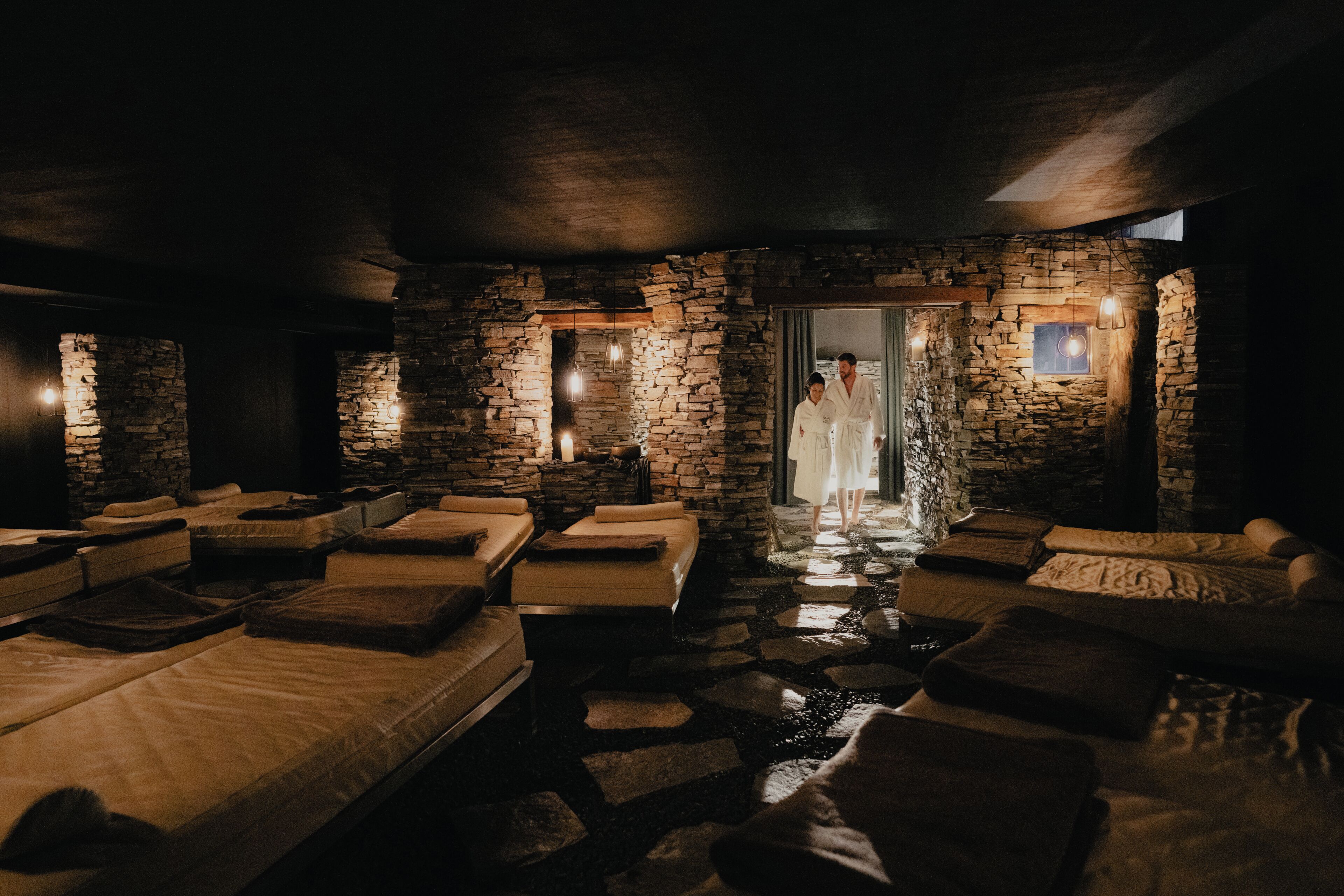 A spa room with stone walls, multiple massage beds, and a person in a robe.