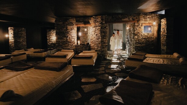 Ein Spa-Raum mit Steinwänden, mehreren Massageliegen und einer Person im Bademantel.