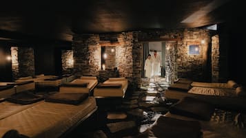 A spa room with stone walls, multiple massage beds, and a person in a robe.