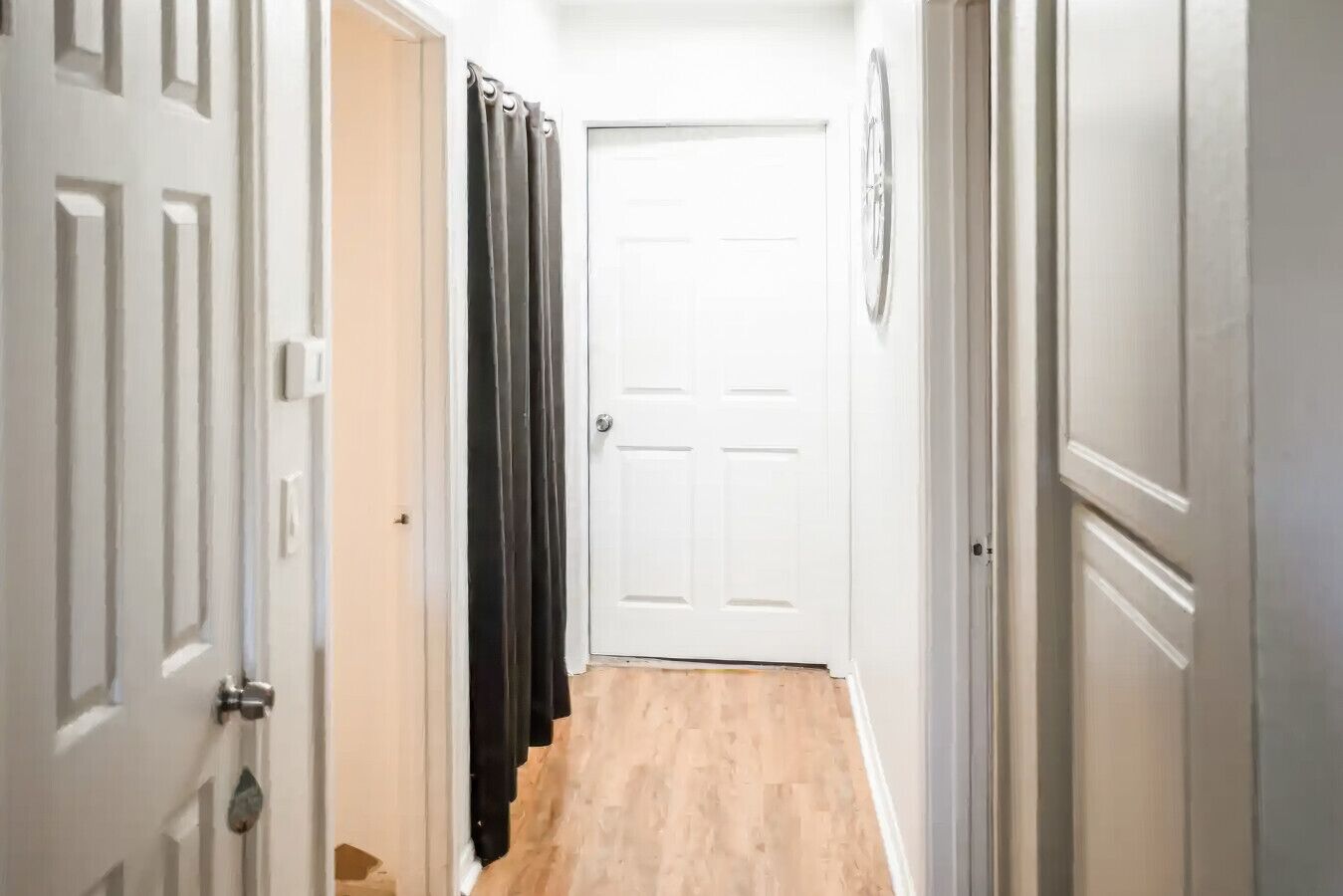 A narrow hallway with wooden flooring, white doors, and a black curtain.